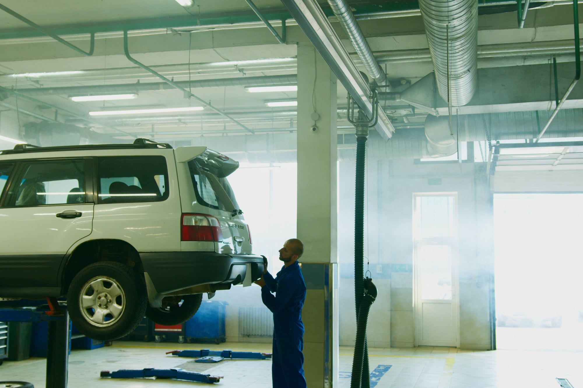A mechanic checks the rear of a car raised on a lift in a bright workshop