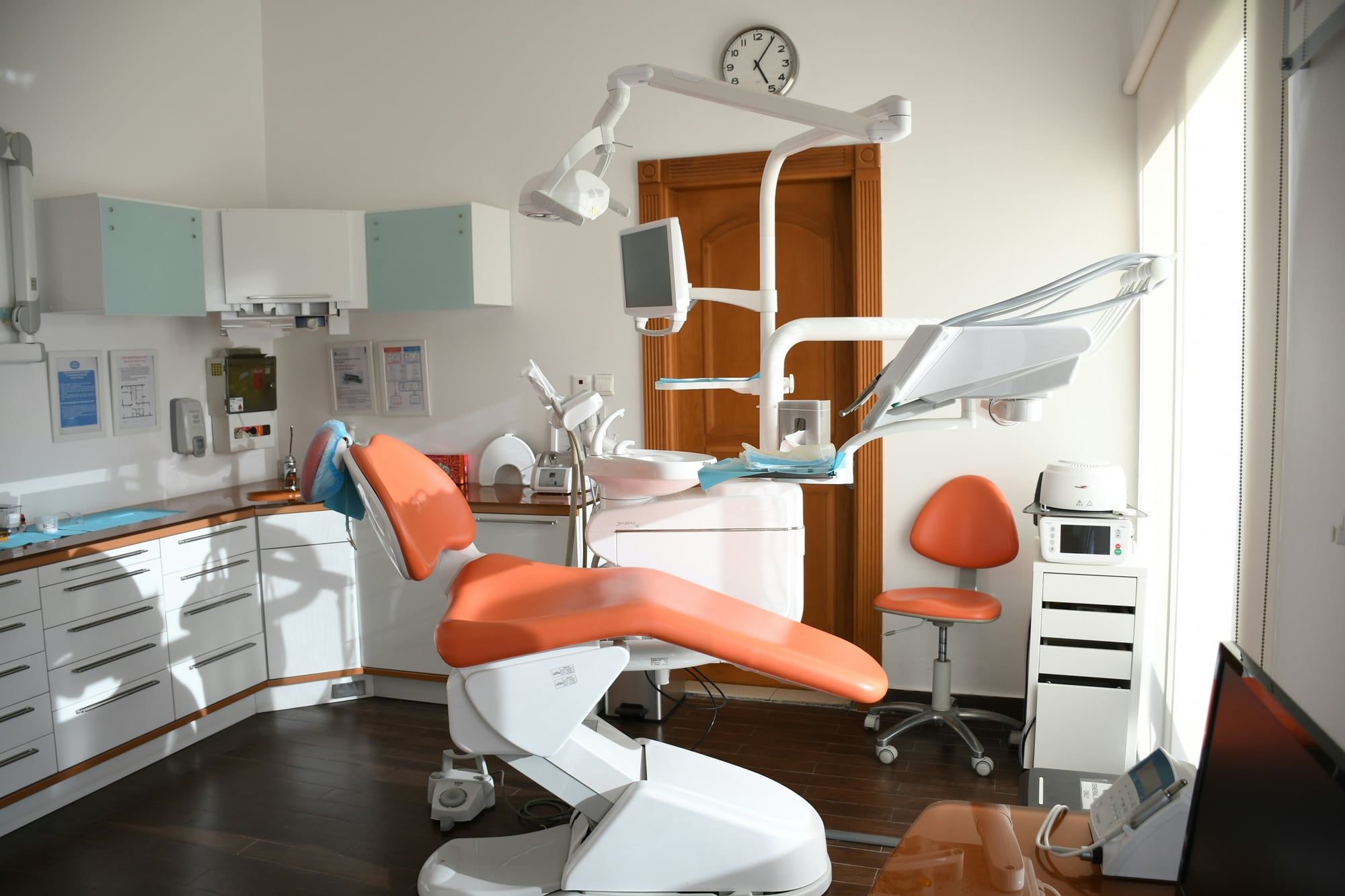 A dental treatment room with an orange chair, lit by daylight from a tall window