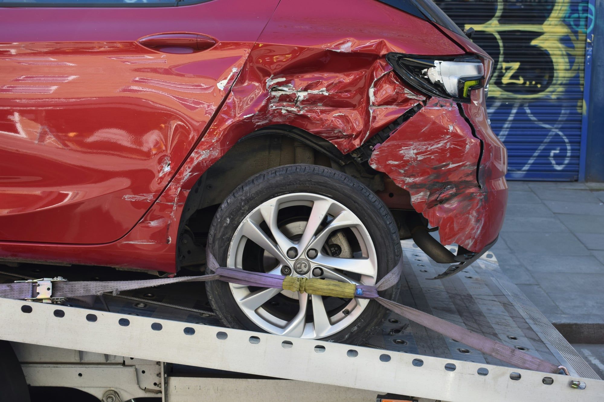 A damaged red car strapped onto the flatbed of a tow truck after a collision