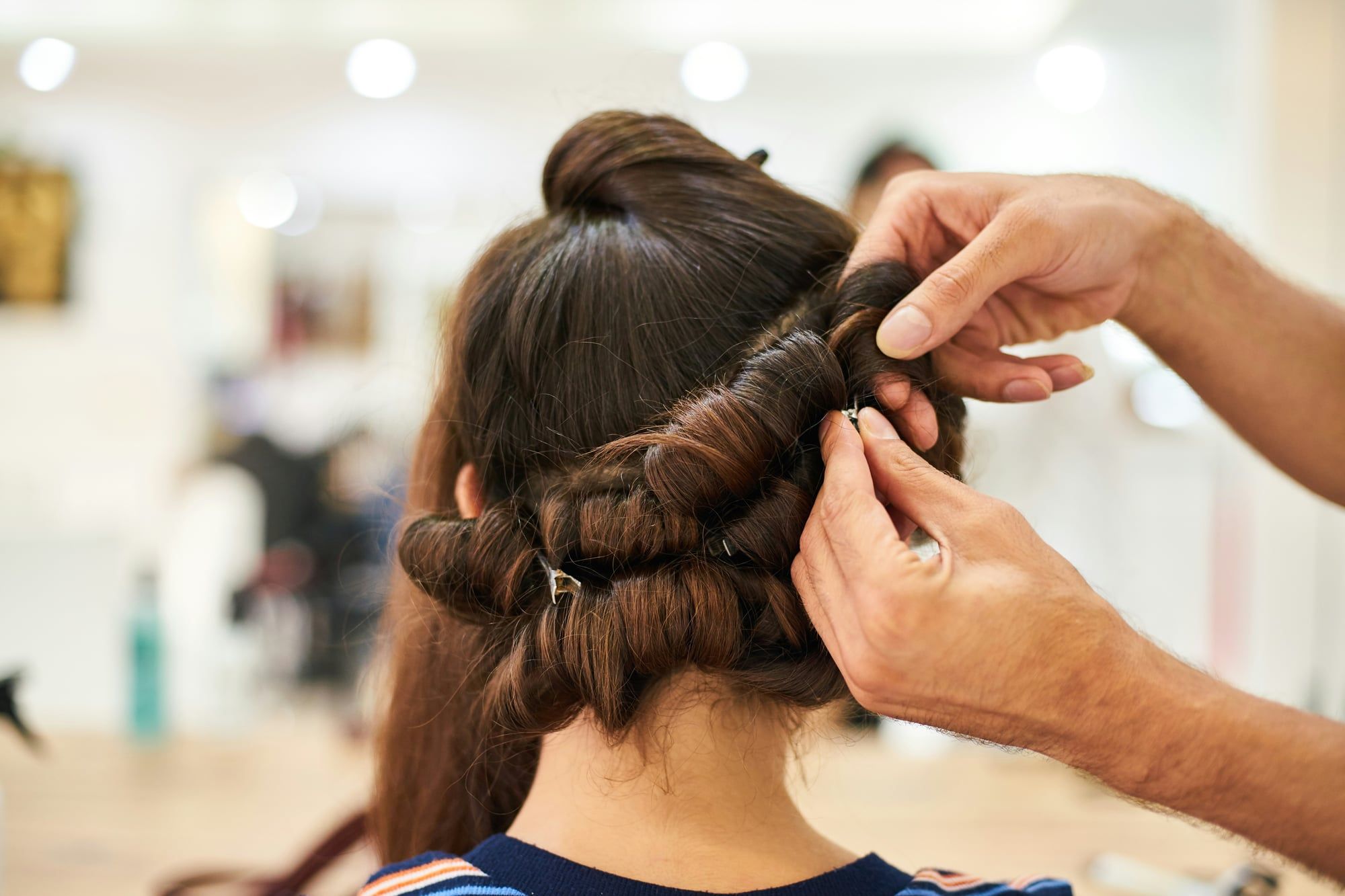 A hairdresser’s hands pin up a client’s hair in a bright salon